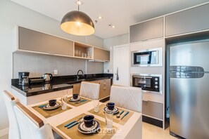 A modern kitchen with built-in appliances, a dining area with a table set for two, and a pendant light above. - MHFs Apartamentos com Vista Mar Itapema (Itapema)
