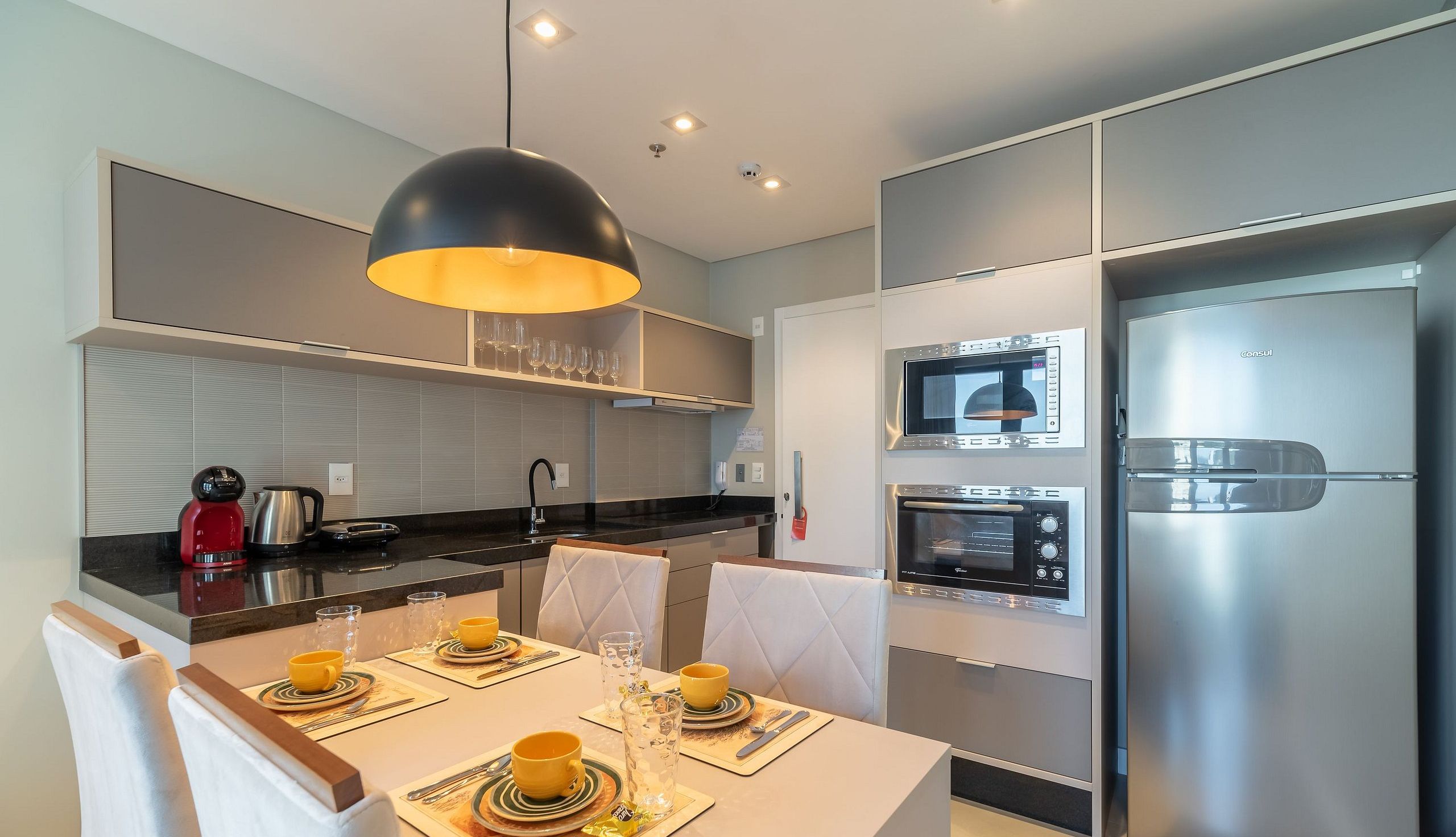 A modern kitchen with a dining area, equipped with a kettle, a coffee maker, and a built-in oven.
