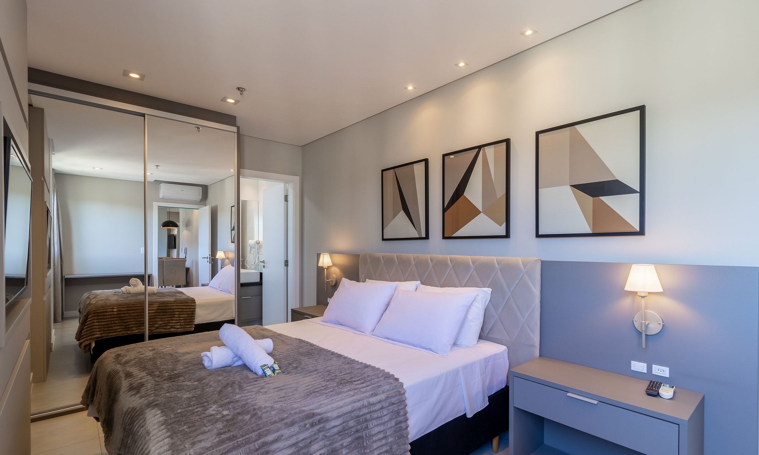A hotel room with a bed, bedside tables, a mirror, and artwork on the wall.