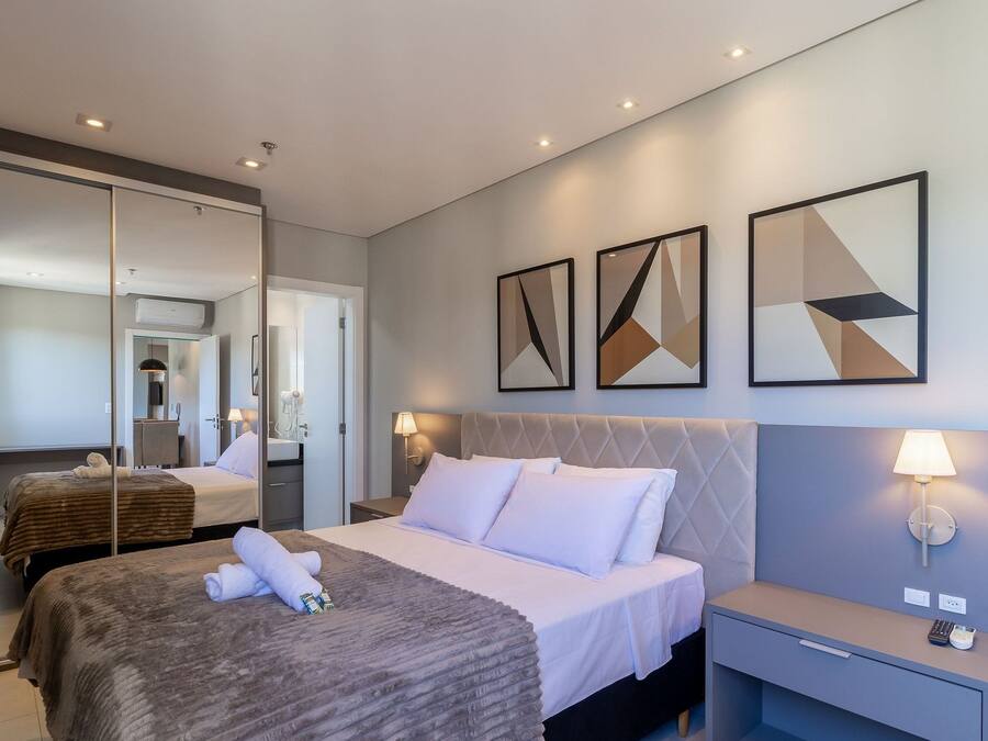 A hotel room with a bed, bedside tables, a mirror, and artwork on the wall.