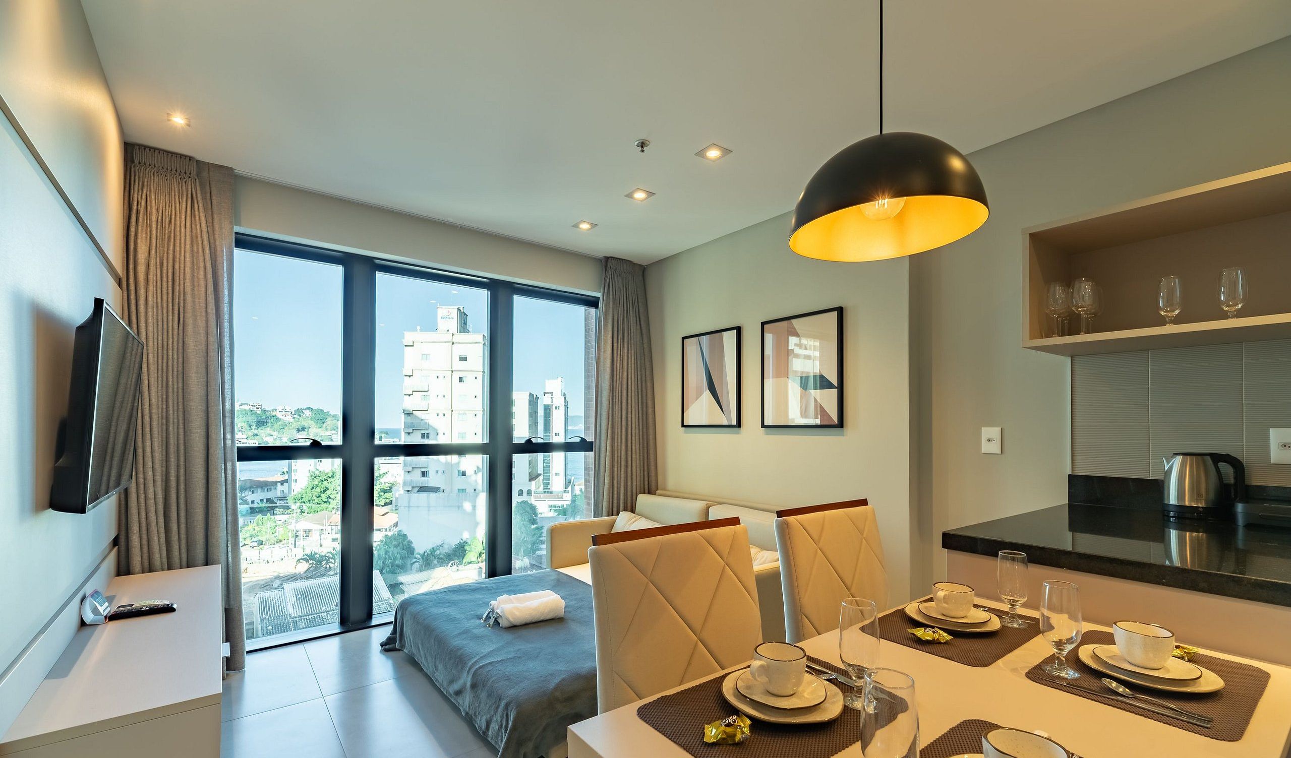 Una habitación de hotel moderna con un ventanal grande, un comedor con una mesa dispuesta para dos personas y una cocina.