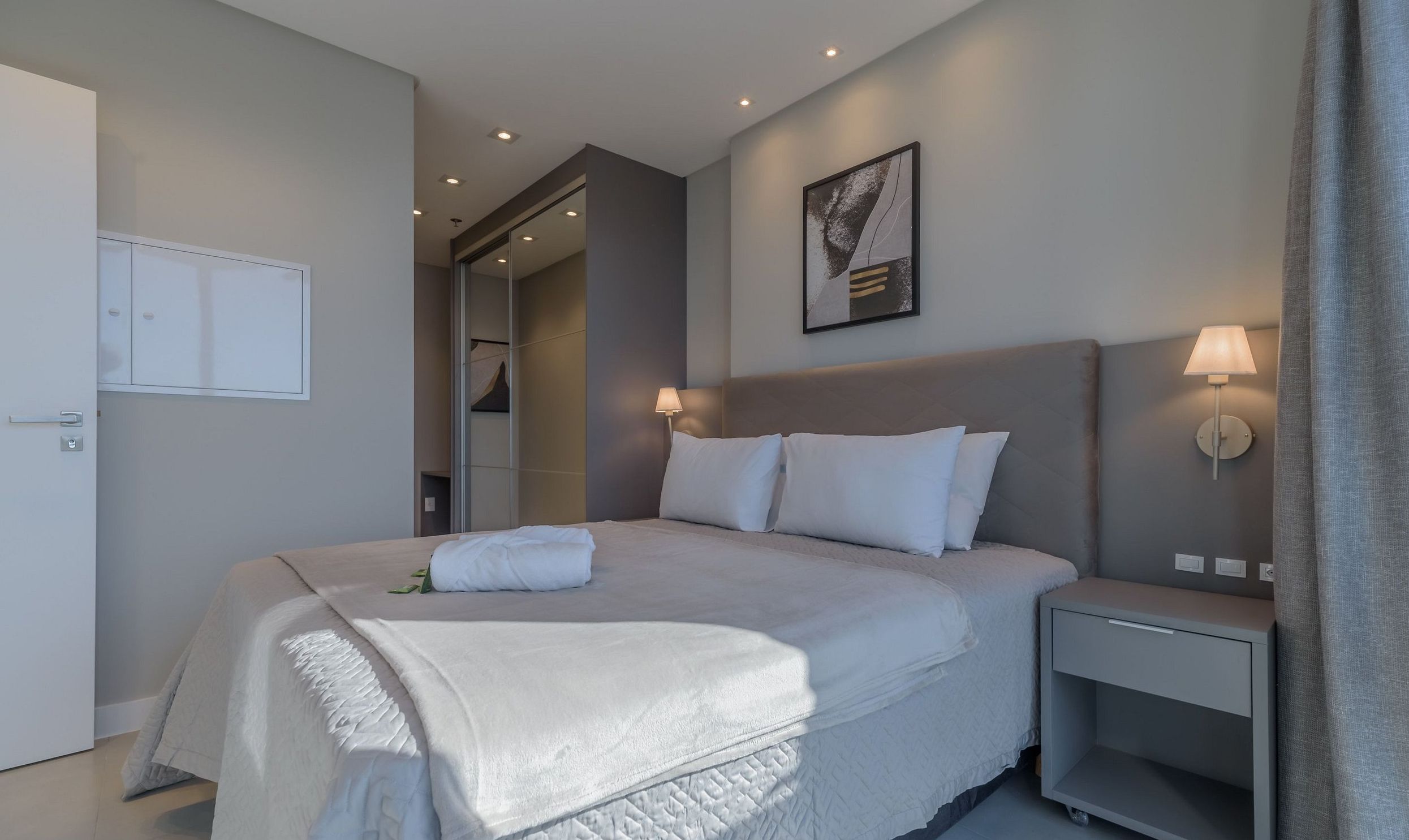 A hotel room with a bed, bedside lamps, a nightstand, a door, and a wall-mounted picture.