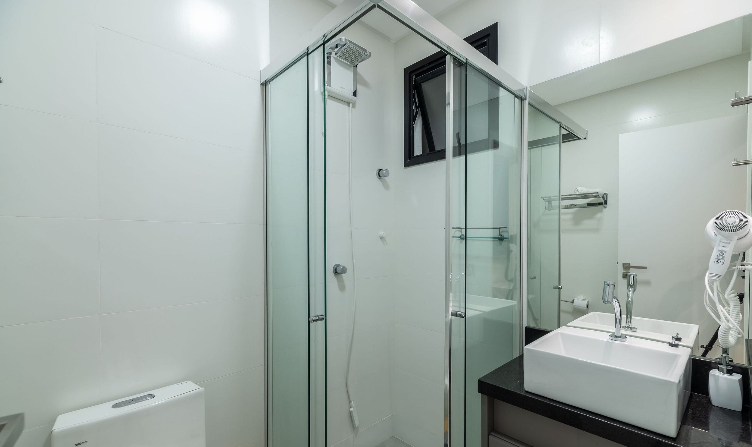 Un bagno moderno con doccia vetrata, lavandino bianco e asciugacapelli.