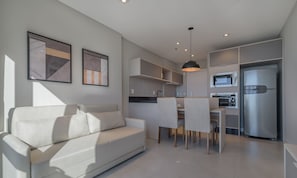 Une cuisine moderne dotée d’appareils électroménagers intégrés, un coin repas avec une table et des chaises, et un canapé blanc.