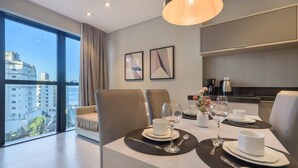 Un espace de restauration moderne avec une table dressée pour deux personnes, une vue sur la ville et une cuisine en arrière-plan.