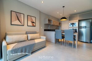 Ein modernes Wohnzimmer mit einer Couch, einem Essbereich mit Stühlen, einer Küche mit Kühlschrank und einer Pendelleuchte.