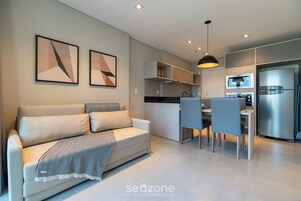 Una sala moderna con un sofá, un comedor con sillas, una cocina con un refrigerador y una lámpara colgante.