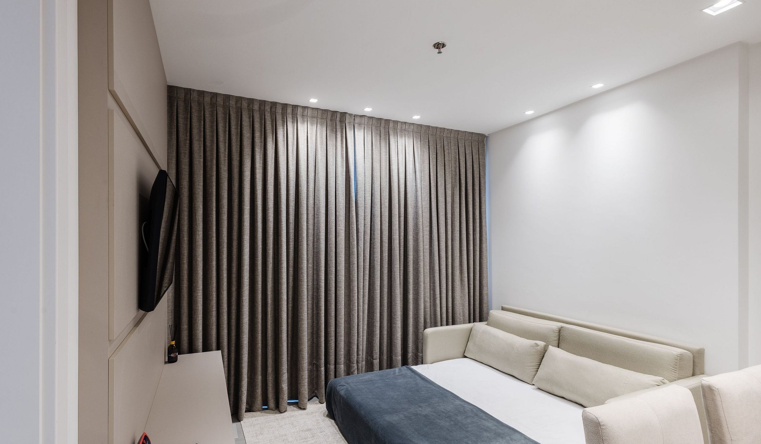 Une chambre à coucher moderne avec un lit, des rideaux, un téléviseur et une petite table.