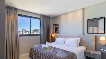 Una camera d'albergo con un letto, un comodino, una lampada, una finestra con tende e vista sulla città.