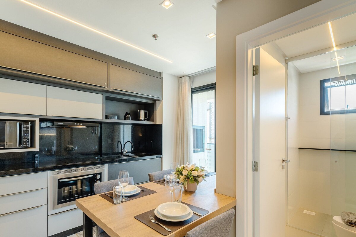 A modern kitchen with built-in appliances, a dining area with a table set for two, and a view of the city through large windows.