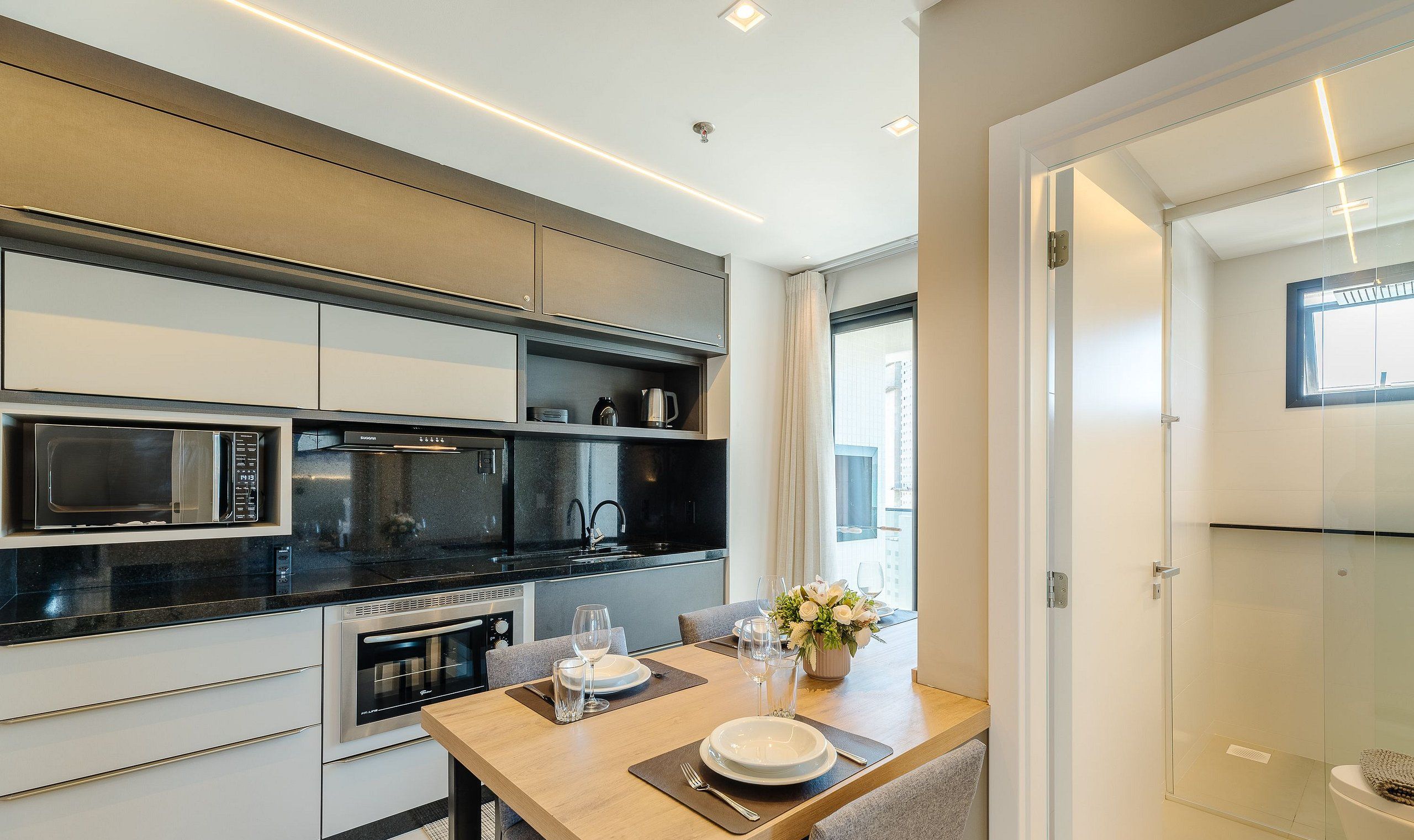 Una cocina moderna con electrodomésticos integrados, una zona de comedor con una mesa lista para dos personas y vistas de la ciudad a través de amplias ventanas.