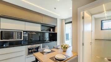 A modern kitchen with built-in appliances, a dining area with a table set for two, and a view of the city through large windows.