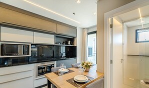 A modern kitchen with built-in appliances, a dining area with a table set for two, and a view of the city through large windows. - MHFs Apartamentos com Vista Mar Itapema (Itapema)