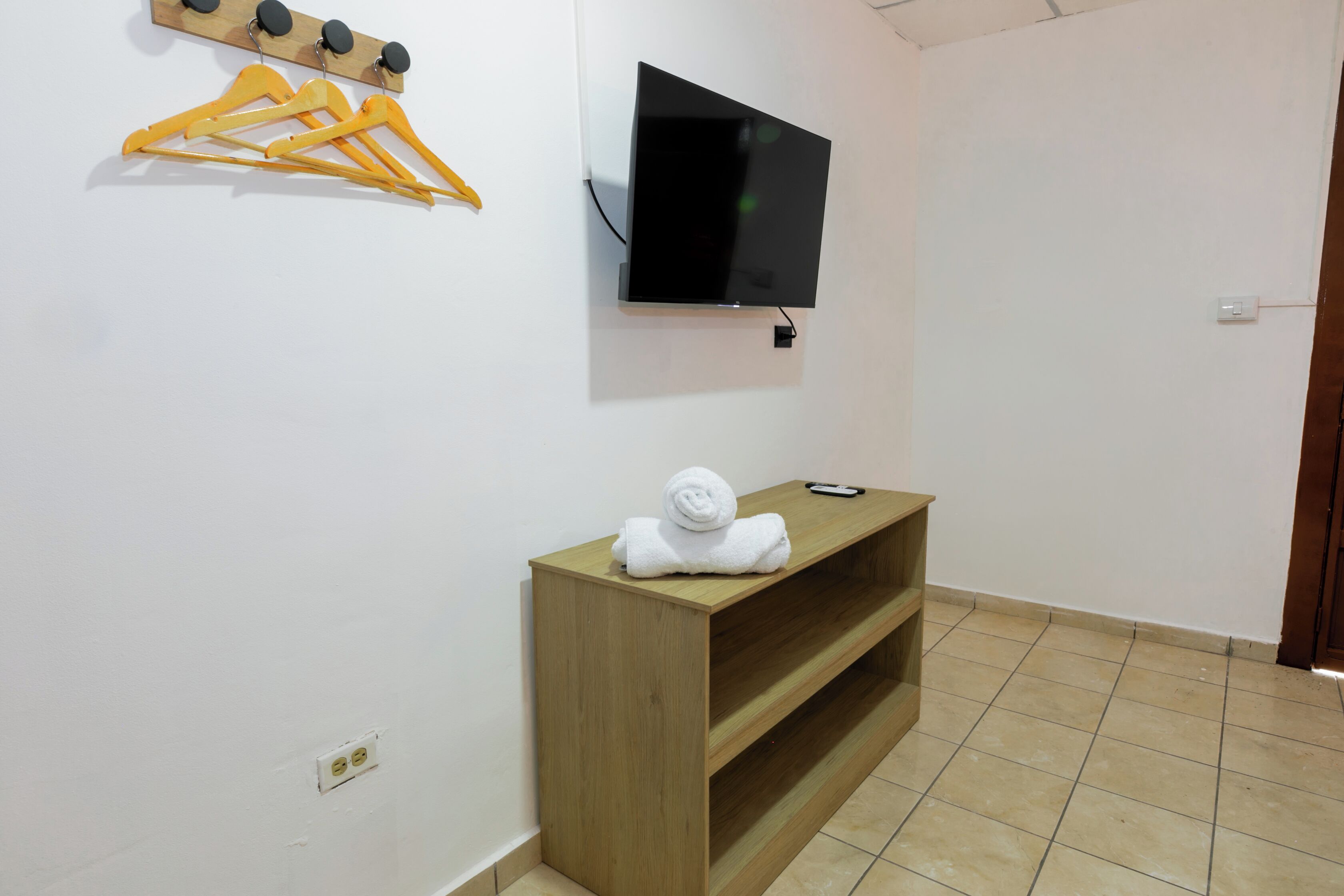 A room with a wooden bench, a flat-screen TV mounted on the wall, and a set of yellow hangers on the wall.