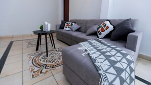 A modern living room with a grey sofa, patterned rug, and a small round table with a plant. - Friendly House (Santa Tecla)