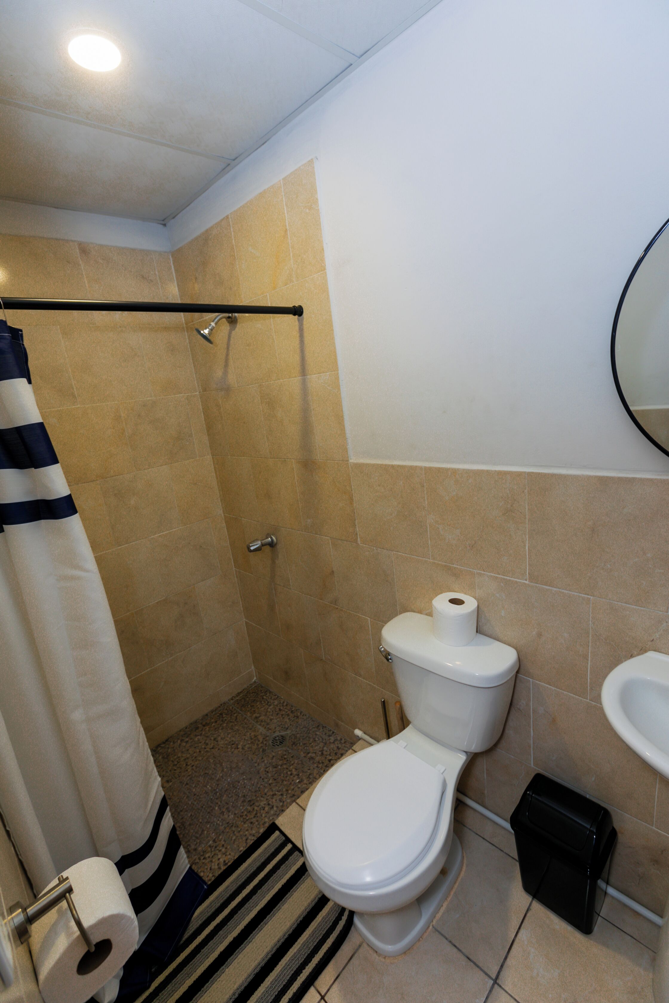 Un baño con ducha, inodoro, lavabo y un perchero a rayas.