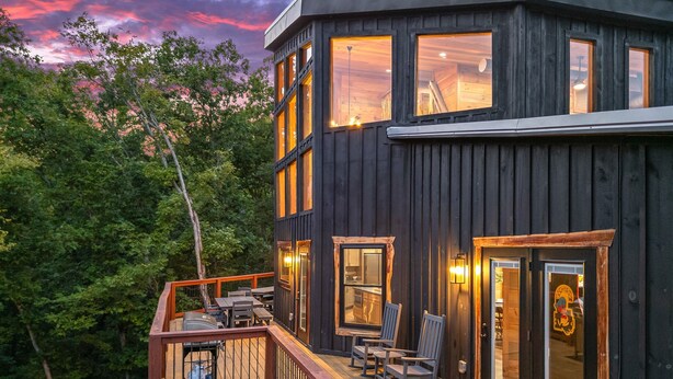 A multi-level wooden cabin with a deck, outdoor seating, and large windows. - NEW Canopy Crest Cabin~Indoor Pool~Hot Tub~Game Room (Sevierville)