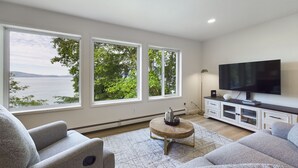 A modern living room with large windows, a flat-screen TV, and a minimalist design. - Lena Beach Oceanview Suite (Juneau)