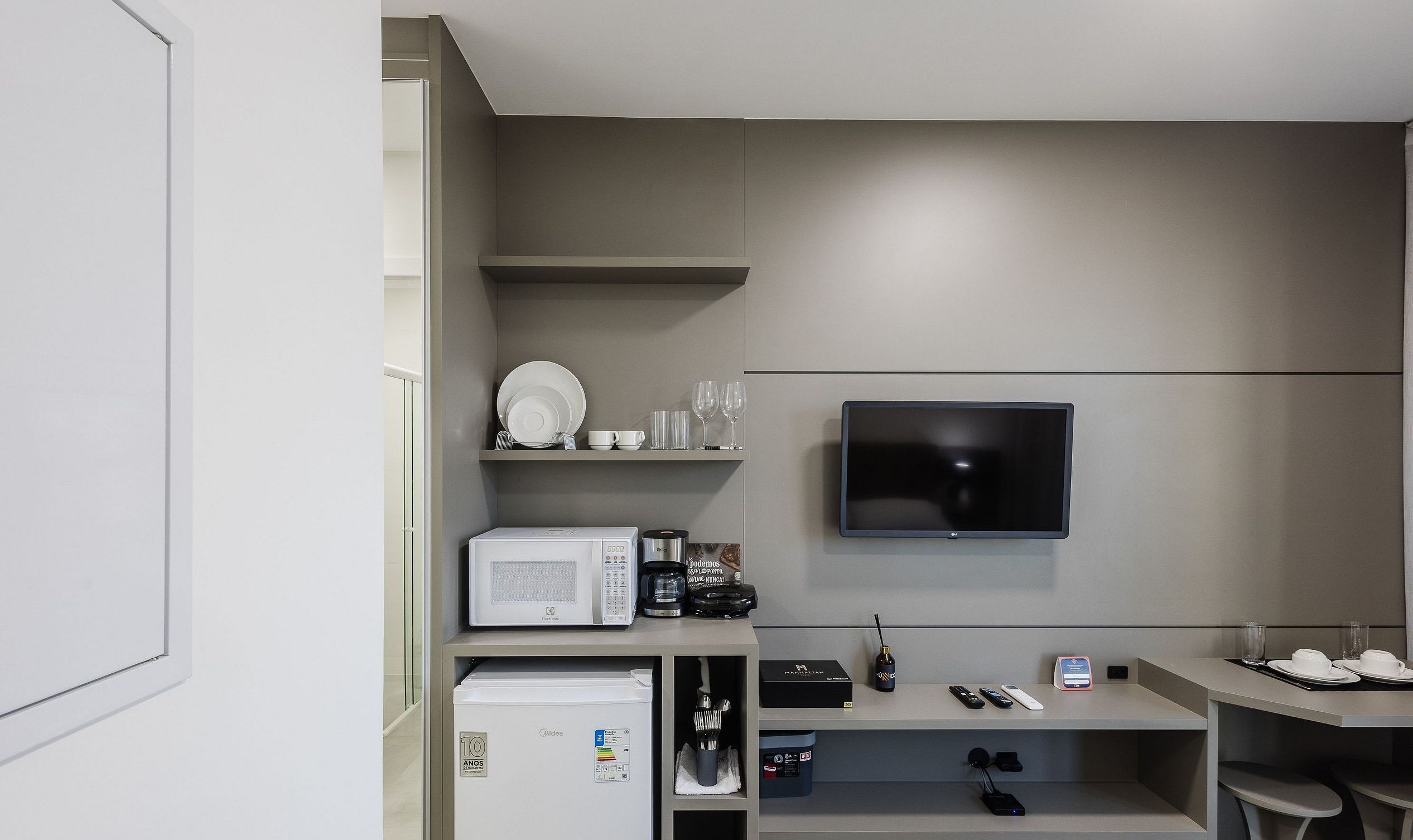 A modern kitchenette with a microwave, coffee maker, and a flat-screen TV mounted on the wall.
