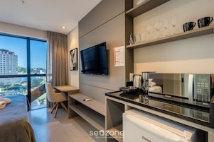 Una habitación de hotel moderna con una cama, un escritorio, un televisor de pantalla plana, un minibar y un ventanal con vistas a la ciudad.
