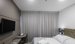 A hotel room with a bed, a desk with a computer, a TV, and a window with curtains. - MHFA Studios em Prédio Luxuoso Vista Mar (Itapema)