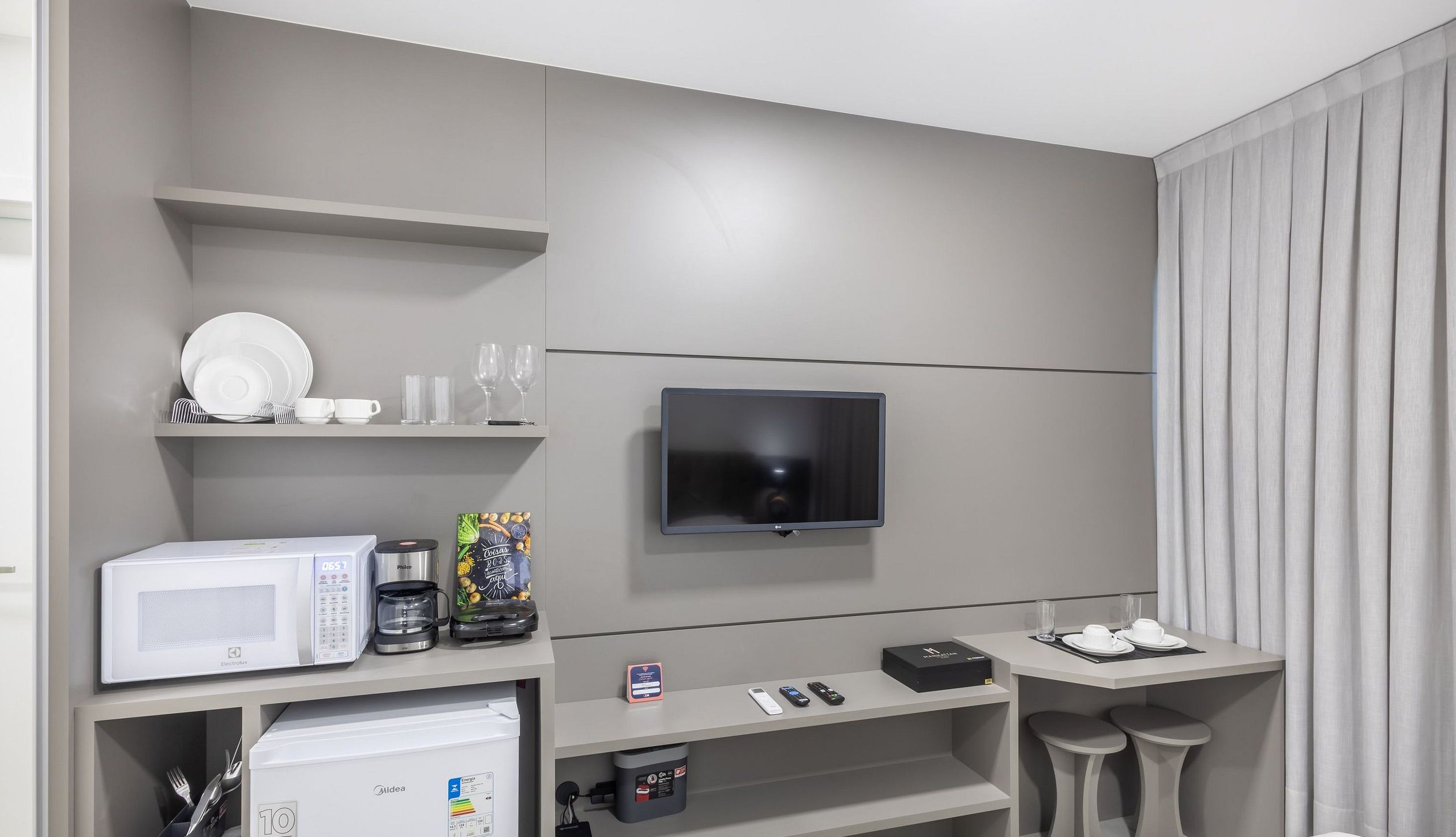 Ein modernes Hotelzimmer mit Flachbildfernseher an der Wand, einer Mikrowelle, einer Kaffeemaschine und einem kleinen Kühlschrank.