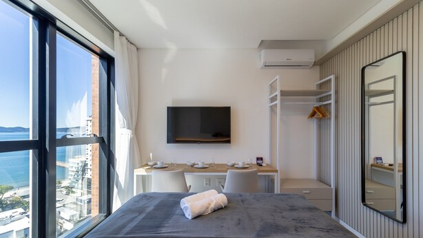 Habitación de hotel con cama, escritorio, televisión de pantalla plana y un gran ventanal con vistas a la ciudad.