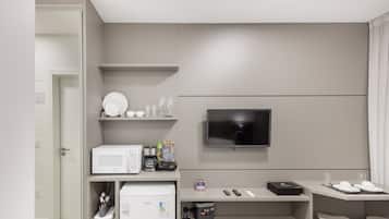 Une chambre d’hôtel moderne équipée d’un téléviseur à écran plat fixé au mur, d’un four à micro-ondes, d’une machine à café et d’une petite table sur laquelle se trouvent une télécommande et un téléphone intelligent.