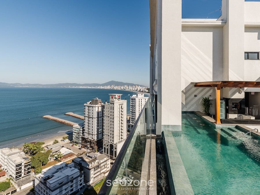 A high-rise building with a pool, overlooking a coastal cityscape.