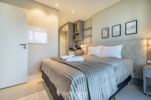 Un dormitorio moderno con una cama grande, un armario, una mesita de noche y un estante en la pared con libros.