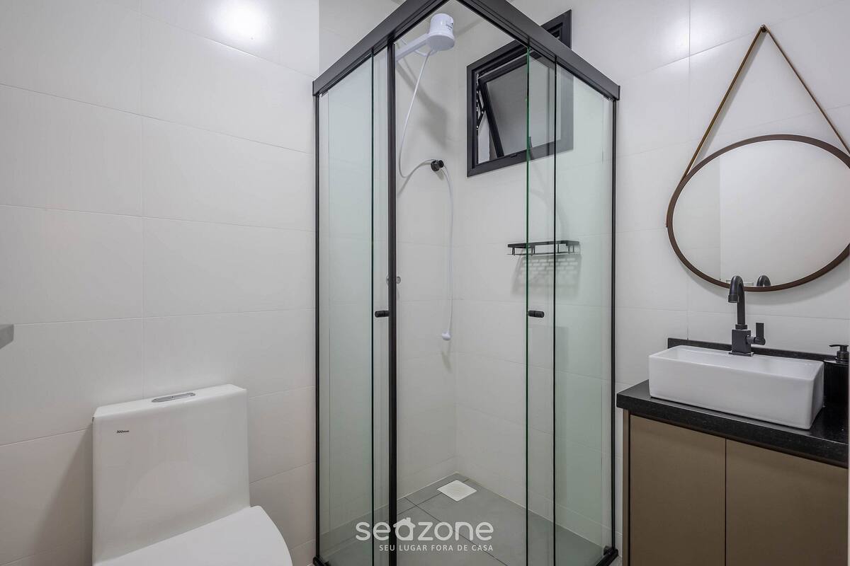 A modern bathroom with a glass-enclosed shower, a white toilet, and a sink with a mirror.