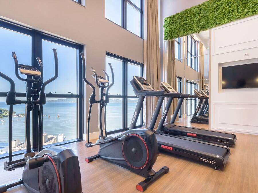 Gimnasio con cintas de correr, bicicletas estáticas y una máquina de remo, con vista a un cuerpo de agua.
