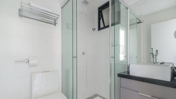 Un baño moderno con cabina de ducha de vidrio, inodoro blanco y tocador con espejo.