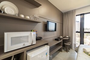 Une chambre d’hôtel moderne équipée d’une télévision à écran plat, d’un four à micro-ondes, d’un mini-réfrigérateur, d’un bureau avec une chaise et d’une grande fenêtre donnant sur la ville.