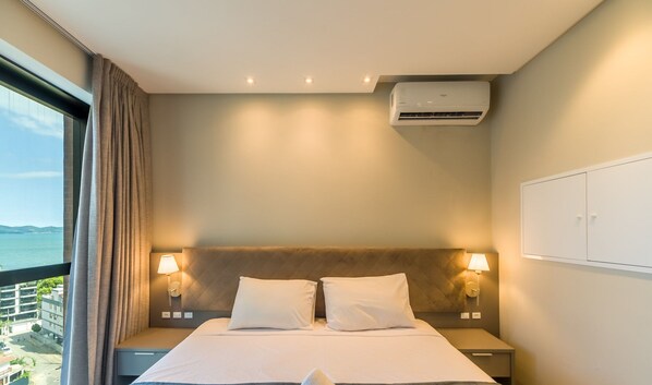 Una habitación de hotel con cama, dos lámparas de noche, aire acondicionado y vista al mar.