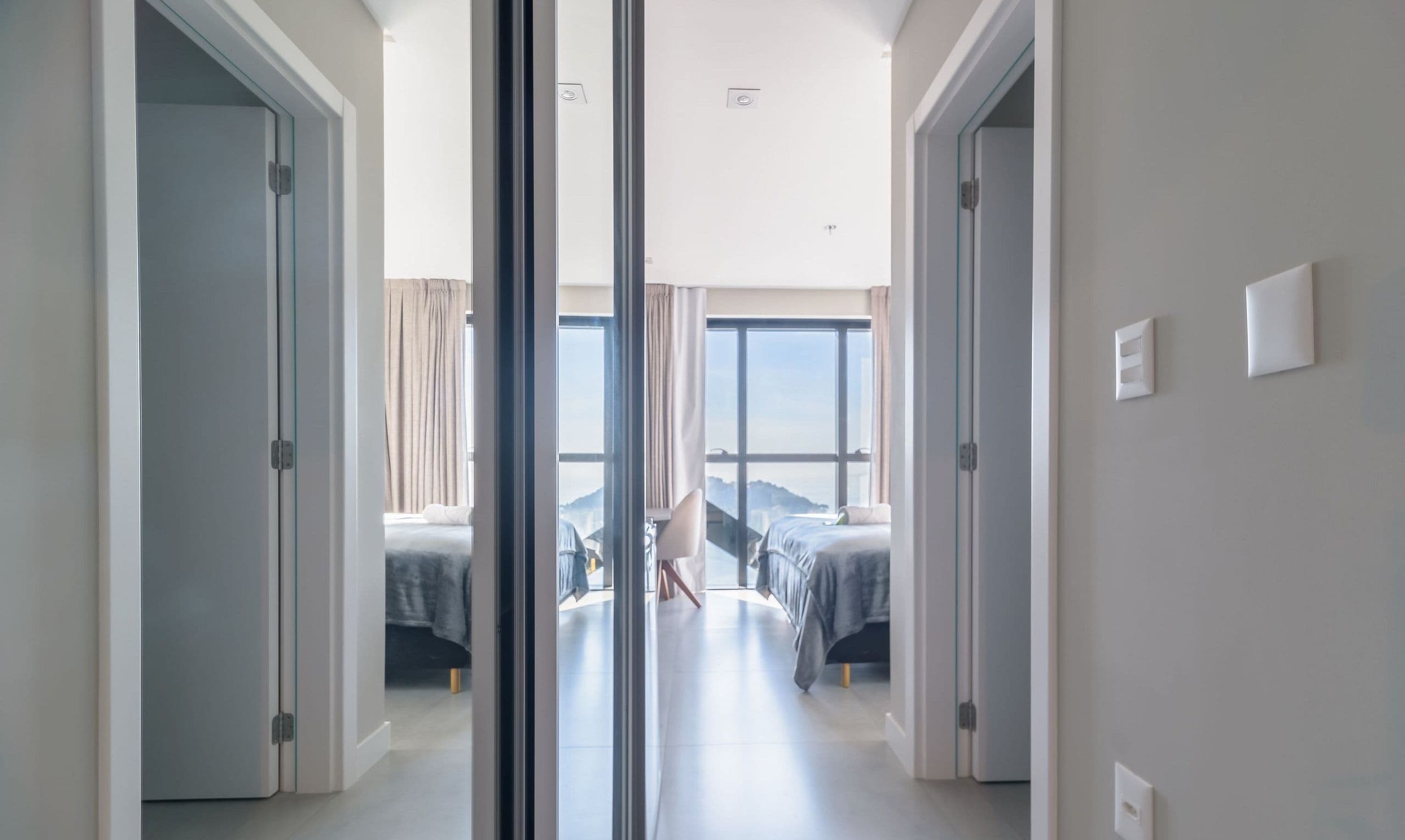 Una habitación de hotel moderna con una cama grande, un escritorio y vistas de la ciudad a través de ventanales de gran altura.