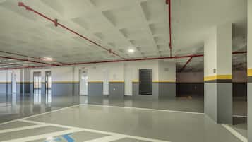 Un amplio estacionamiento interior con líneas de techo definidas, tuberías rojas y un camino accesible para sillas de ruedas.