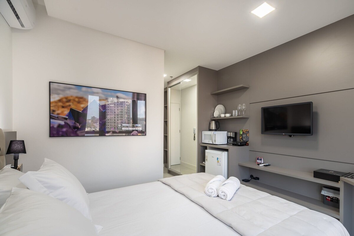 Una habitación de hotel con una cama, un televisor de pantalla plana, un minibar y un cuadro en la pared.