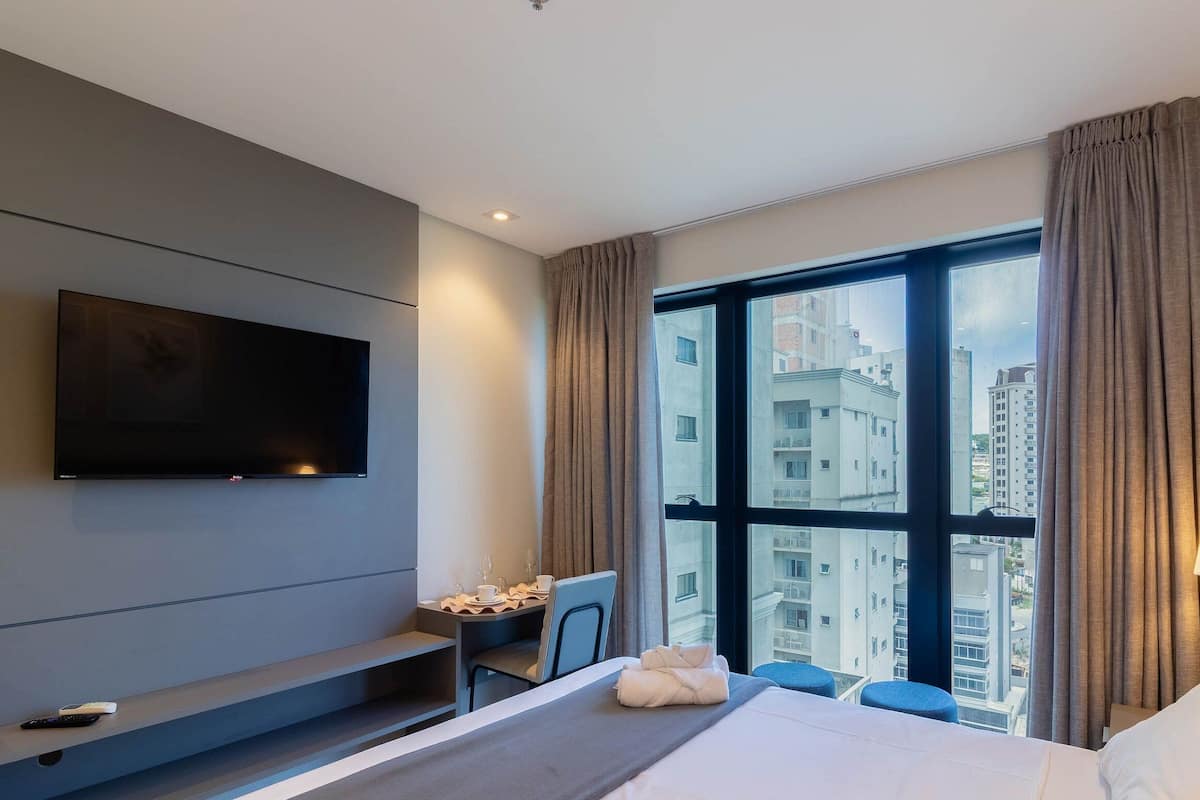 A hotel room with a bed, a desk, a chair, a TV, and a large window with curtains.