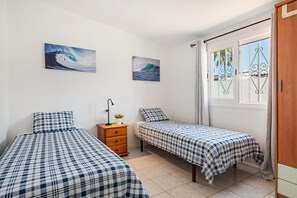 Quarto com duas camas, uma cômoda e duas pinturas na parede.