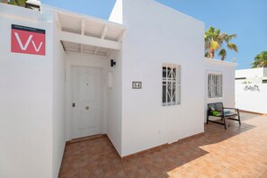 Un edificio bianco con una porta, una finestra con sbarre, un segnale con un numero e una panchina.