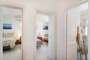 Una camera da letto con un letto, un comodino, una lampada e vista su un'altra stanza.