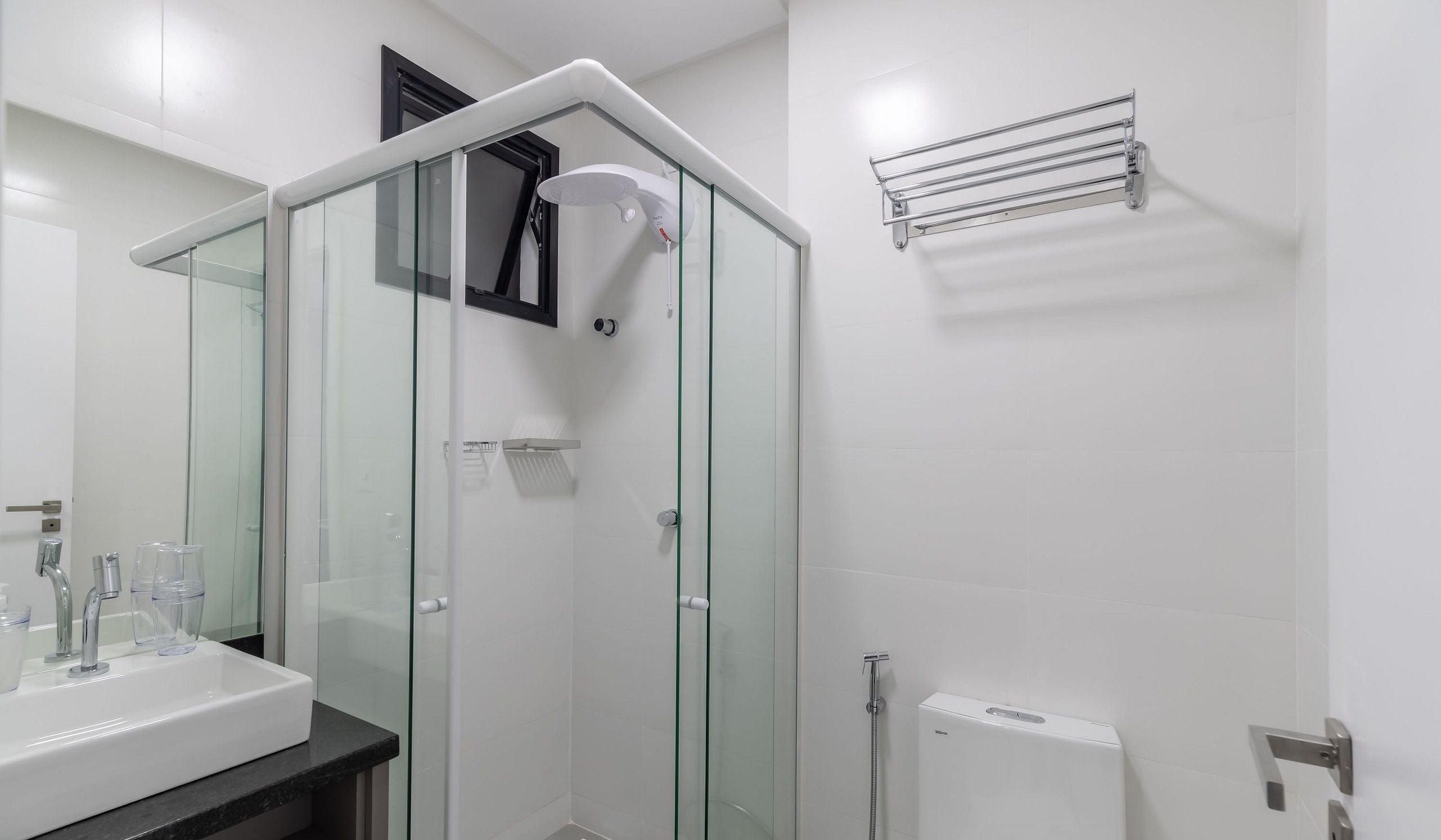 Un baño moderno con cabina de ducha de vidrio, un lavabo blanco y un perchero para toallas.