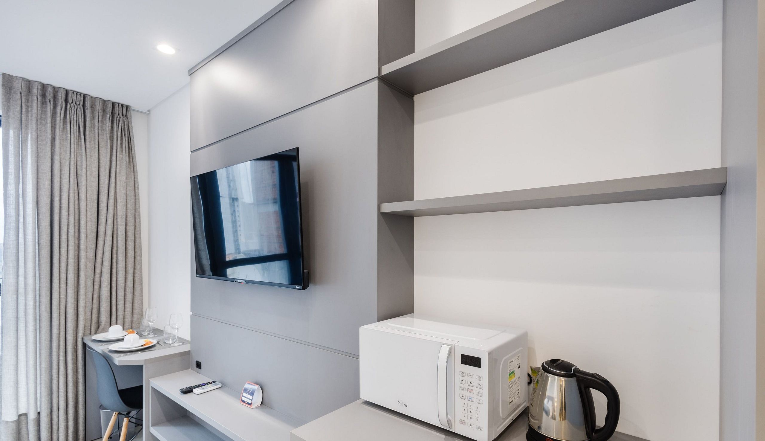 Quarto de hotel moderno com televisão de tela plana na parede, micro-ondas branco e chaleira no balcão.