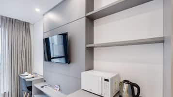 Quarto de hotel moderno com televisão de tela plana na parede, micro-ondas branco e chaleira no balcão.