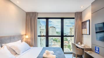 Habitación de hotel con cama, escritorio, silla, televisor y vista panorámica de la ciudad.