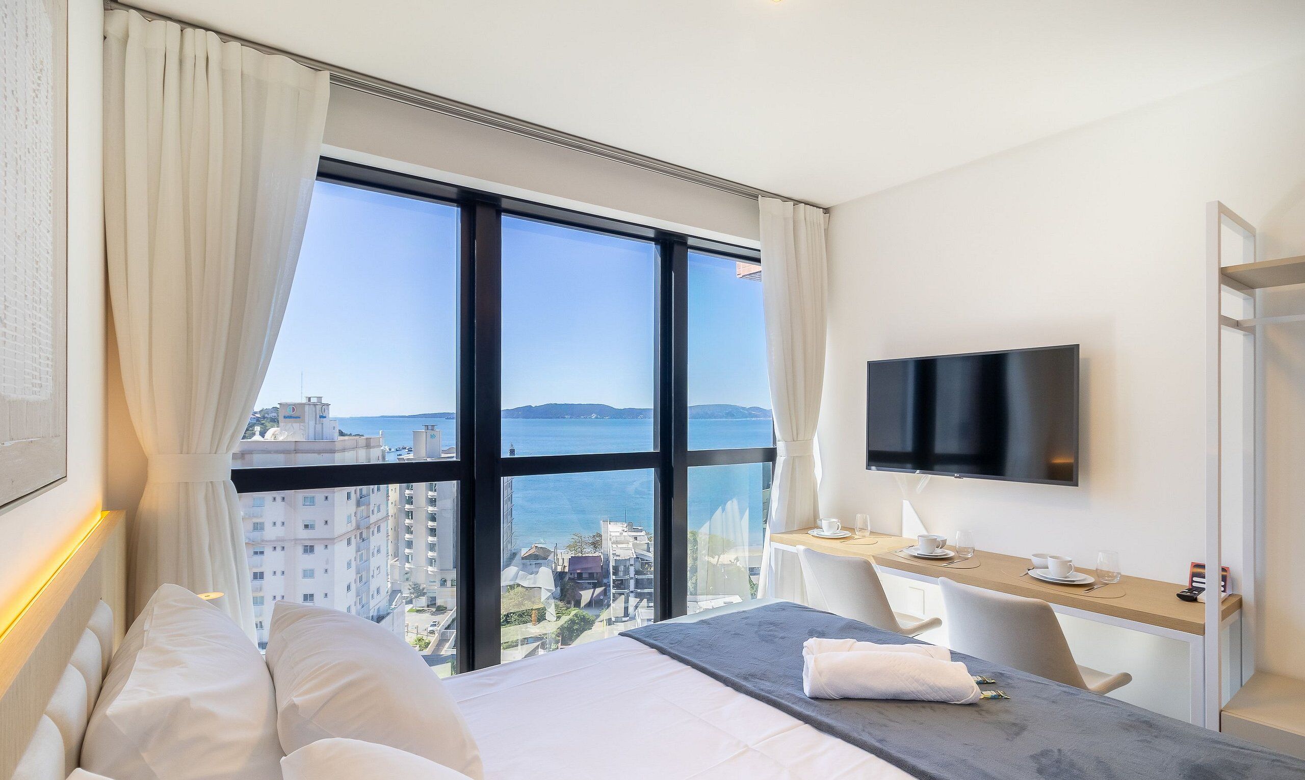 Une chambre d’hôtel avec une grande fenêtre, un lit, un bureau et une télévision.