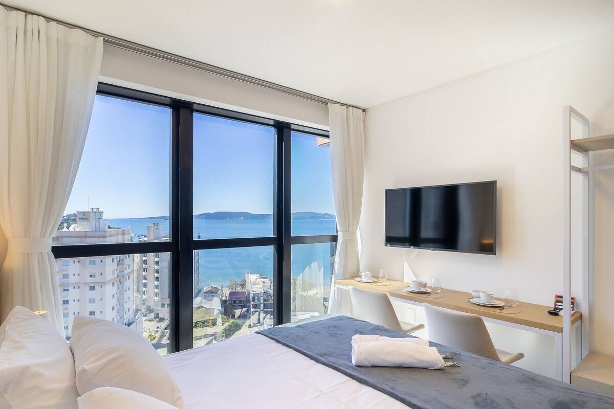 Une chambre d’hôtel avec une grande fenêtre, un lit, un bureau et une télévision.