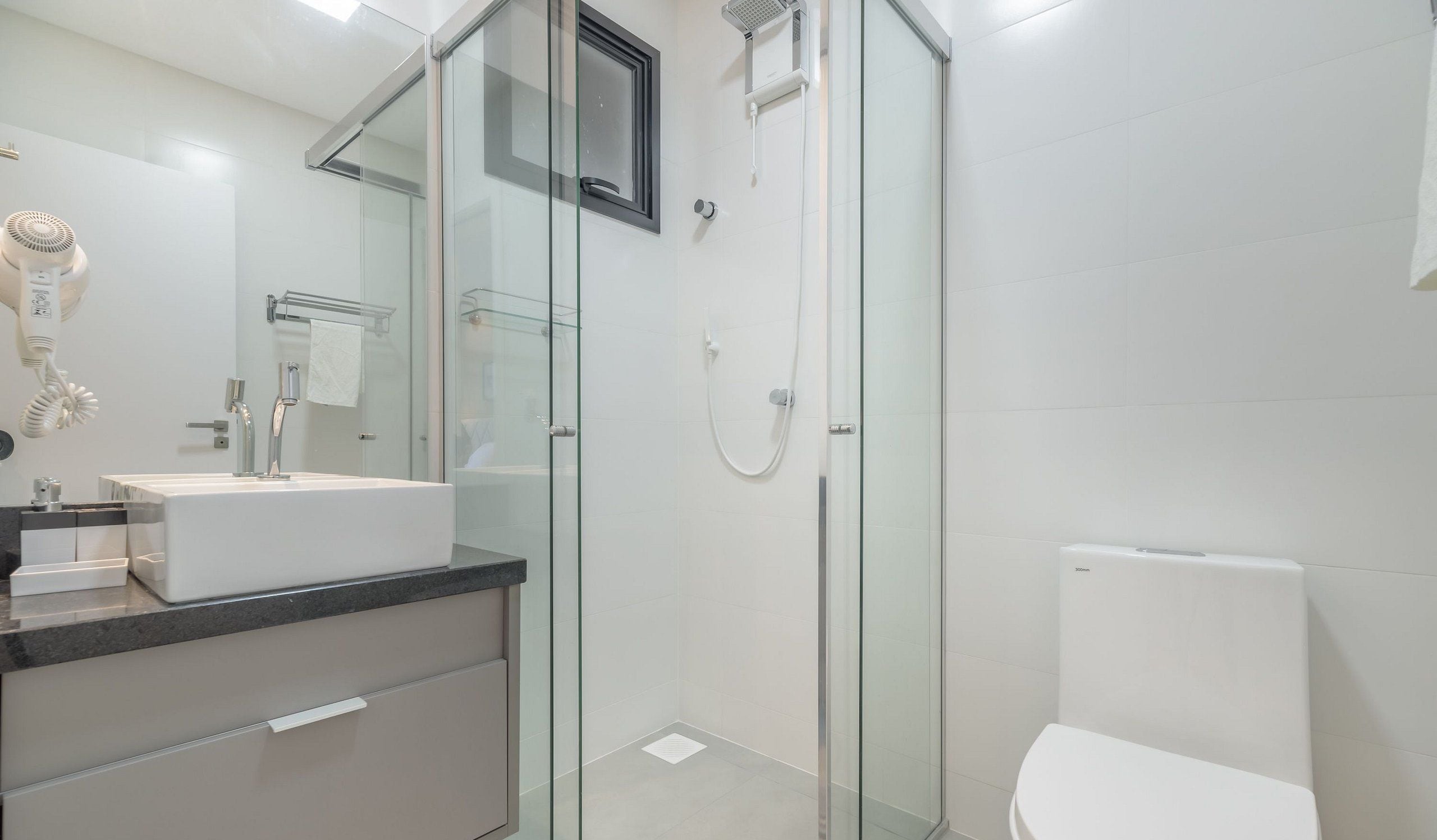 A modern bathroom with a glass-enclosed shower, a white toilet, and a vanity with a mirror and a hairdryer.