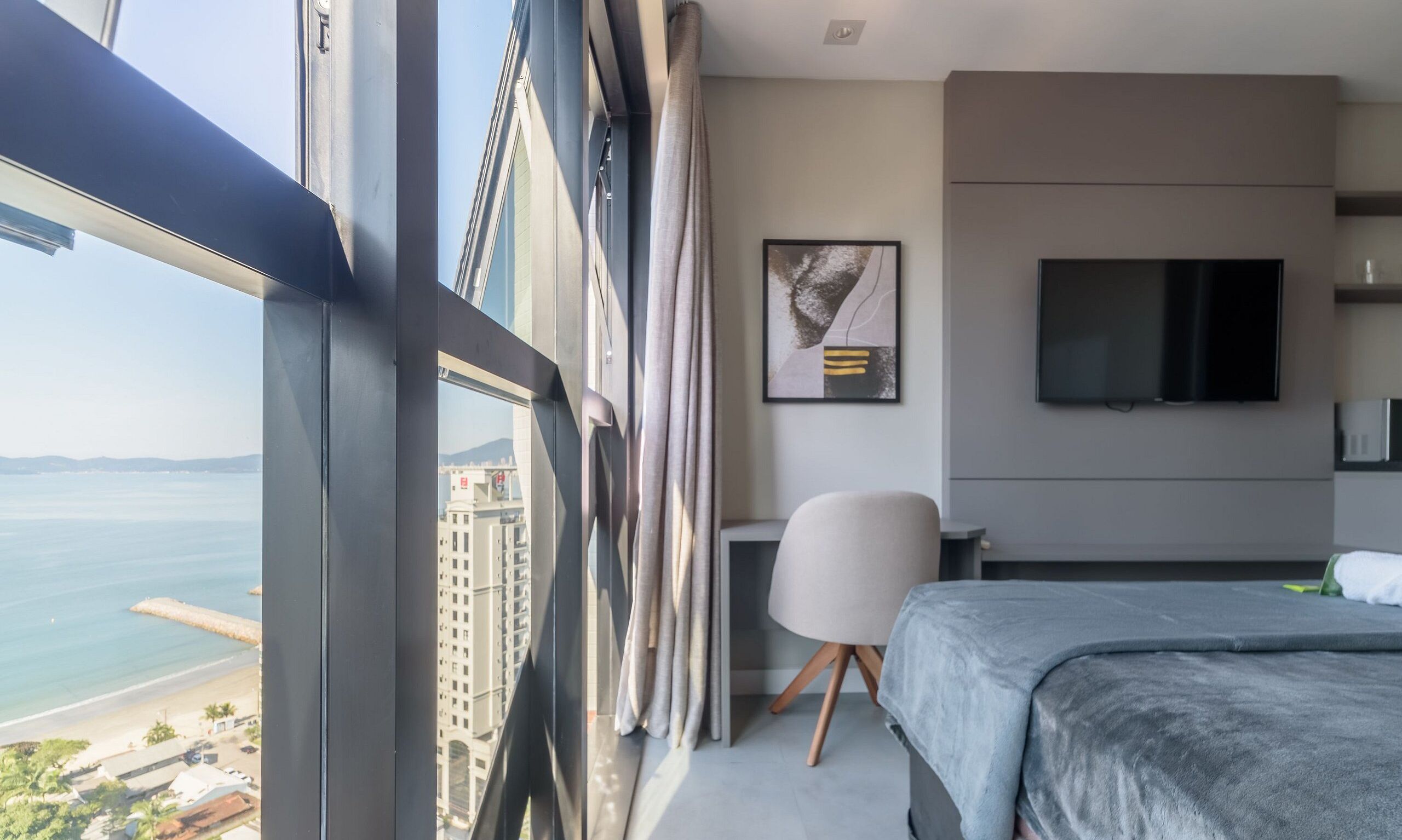 Une chambre d’hôtel moderne dotée d’une grande fenêtre, d’un lit, d’un bureau et d’une télévision.
